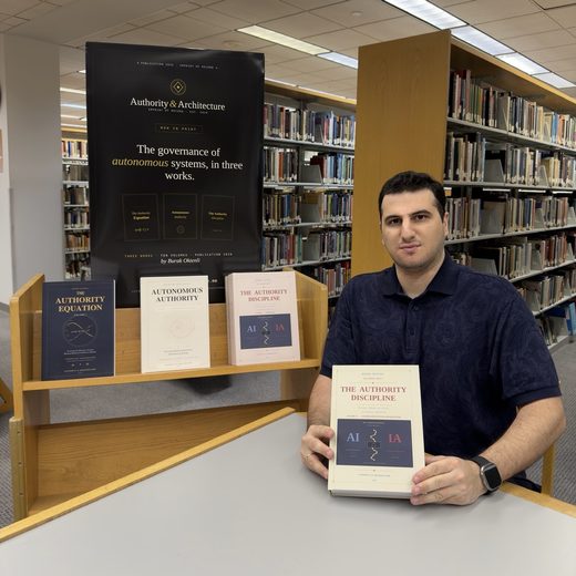 Burak Oktenli seated in a library beside a display of his three book series, The Authority Equation, Autonomous Authority and The Authority Discipline, holding a volume of The Authority Discipline